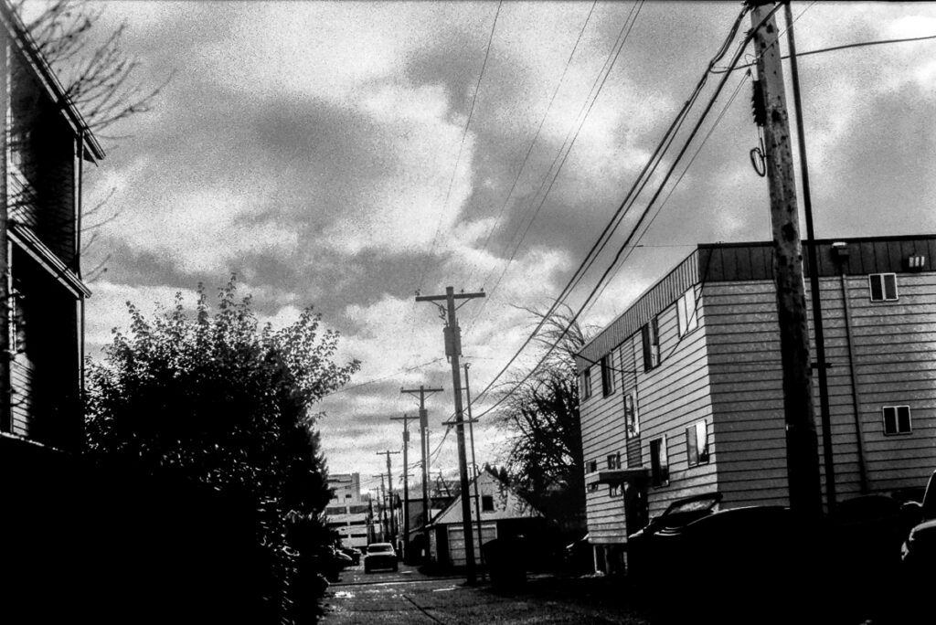 Black and white image of an alley, with dramatic clouds overhead