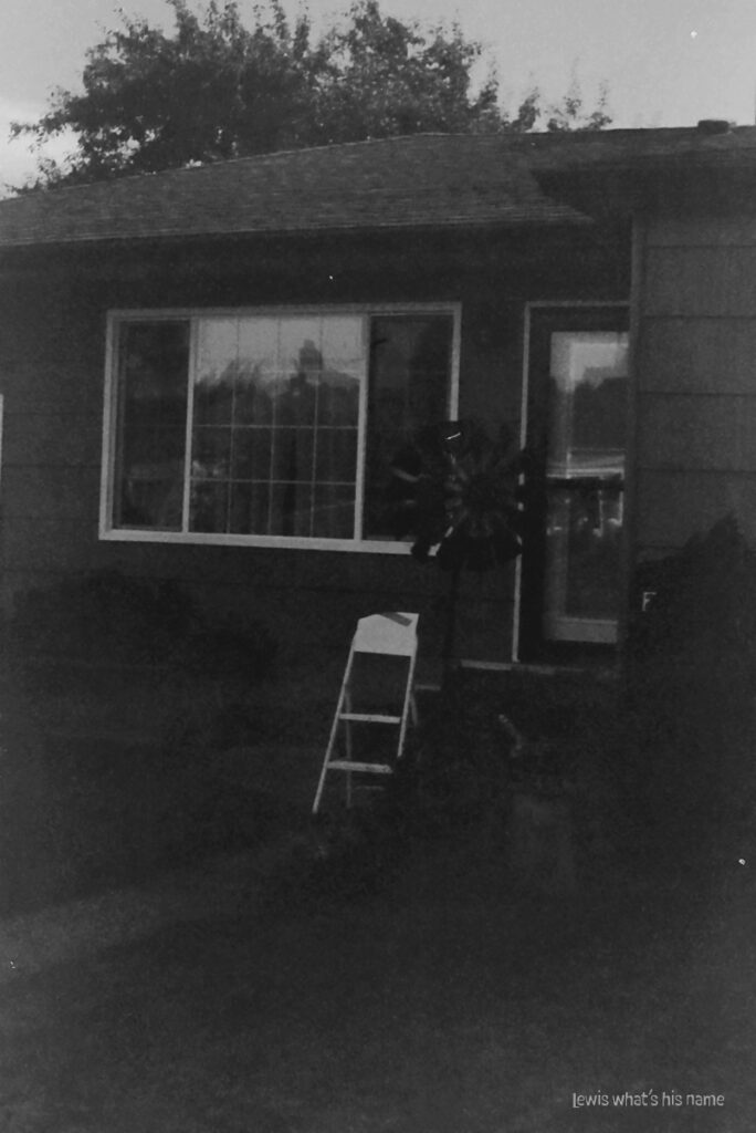 Black and white image of a house, with a small ladder in the path to the front door.  Everything is poorly exposed and foggy.